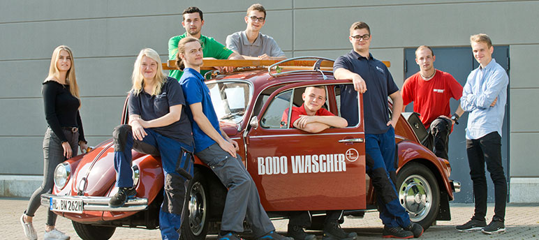 Auszubildende der Bodo Wascher Gruppe stehen um den Wascher VW Käfer verteilt